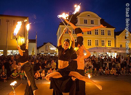Altstadtfest Beilngries (Naturpark Altmühltal) Feuershow mit vier Akrobaten und Publikum auf einem Platz vor beleuchteten Gebäuden bei Nacht.